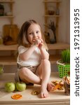 Small photo of cute little girl eats natural pastille at home in a wooden kitchen. Food for children from natural products
