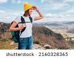 Young happy smiling woman, wears yellow beanie and backpack, hiking in the mountains. Top view, landscape, adventure concept.