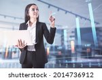 Attractive young european businesswoman with laptop and abstract forex chart standing on blurry background with mockup place. Technology, trade and finance concept. Double exposure