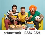 Small photo of Excited three male friends watch sport tournament, have bated breath during dangerous moment, bite crisps popcorn and pizza sit on yellow sofa in living room. Soccer fans with beer. Football supporter