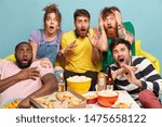 Small photo of Scared group of friends watch horror movie, feel great fear and surprise during thrilled scary film moment, have bated breath, eat junk food, spend lazy day off together sit on couch against blue wall