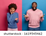 Small photo of Angry curly haired woman shouts with reproach, bearded emotional man raises palms with hesitation and puzzlement express different emotions stand against bright two colored background. Color contrast