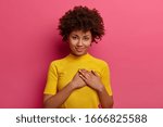 Sign of affection and admiration. Pretty curly woman presses palms to heart, being grateful for gift, wears yellow t shirt, poses over rosy background, says you are always in my heart, smiles gently