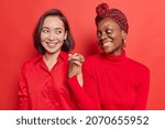 Small photo of Friendship sign. Happy women shake hands together being best fiends reconcile with each other after quarrel smile gladfully isolated over bright red background wear casual clothing pose indoor