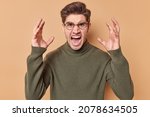 Small photo of Outraged man gestures angrily raises shakes hands and screams loudly expresses fury has fight with wife wants to get divorce dressed in casual jumper isolated over beige background. Feel my fury