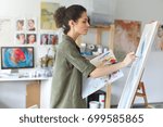 Pretty talented female painter painting on easel, making colorful sketches, creating marine landscape. Beautiful female artist painting with watercolor paints. Creativity and imagination concept