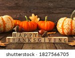 Happy Thanksgiving greeting on wooden blocks against a rustic wood background with pumpkins and autumn leaves
