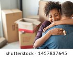 Young african woman holding home keys while hugging boyfriend in their new apartment after buying real estate. Lovely girl holding keys from new home and embracing man. Couple around cardboard boxes.