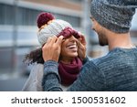 Loving multiethnic couple having fun outdoor in winter. Young man covering eyes his girl with woolen cap. Cheerful guy and smiling african woman playing in winter outdoor.