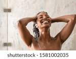 Young woman washing hair in shower at luxury spa. Woman washing her curly hair with shampoo and a lot of lather. Carefree black girl taking a long hot shower washing her hair in a modern bathroom.