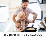 A small boy with father indoors in kitchen making pancakes.