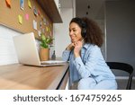 Smiling young african american teen girl wear headphones video calling on laptop. Happy mixed race pretty woman student looking at computer screen watching webinar or doing video chat by webcam.