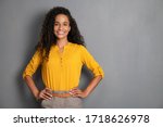 Portrait of young african woman standing with hands on waist and looking at camera. Confident stylish girl standing against grey background. Happy young mixed race woman smiling i with copy space.