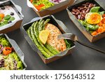 Ready healthy food catering menu in lunch boxes fish and vegetable packages as daily meal diet plan courier delivery with fork isolated on black table background. Take away containers order concept.