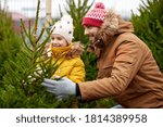 family, winter holidays and people concept - happy father and little daughter choosing christmas tree at street market