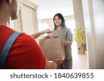 Indian woman customer taking delivery paper eco bag with grocery takeout food meal from man courier holding paper package delivering supermarket or restaurant takeaway order standing at door at home.