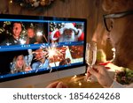 Young man wears Christmas hat drinking champagne holding sparkler talking to friends on virtual video call celebrate Happy New Year party in distance online chat at home, over shoulder screen view.