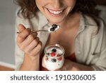 Close up of of smiling woman having a healthy breakfast at home with fruit and yogurt. Girl tasting yoghurt with blueberries and raspberries. Woman enjoy fresh yogurt for lunch, wellbeing diet concept