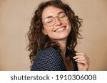 Casual cheerful woman with eyeglasses smiling at camera on cream background. Close up of happy young woman laughing with eyeglasses. Beautiful girl having fun with closed eyes showing a big grin.