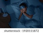 people, relax and comfort concept - young african american woman in eye mask sleeping in bed at home at night