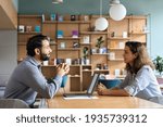 Small photo of Indian male hr specialist manager, employer, boss listening female latin candidate at job interview, consulting client at office meeting. Hiring and employment, human resources, recruitment concept.