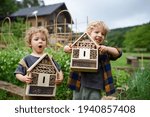 Small boy and girl holding bug and insect hotel in garden, sustainable lifestyle.
