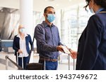 Indian passenger wearing protective face mask showing e-ticket to flight attendant at boarding gate. Mixed race businessman showing boarding pass on mobile phone to air hostess during covid pandemic.