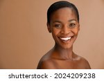 Beautiful middle aged woman with perfect skin looking at camera against a brown background. Portrait of black beauty woman smiling in studio with smooth complexion flawless skin. Mature african lady.