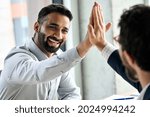 Indian happy smiling multiracial professional ceo businessman giving highfive to business partner after financial acquisition bank bargain contract at office. High five concept. Over shoulder view.