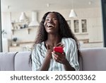 Excited happy young black African woman shopper winner holding cell phone laughing feeling joy getting mobile message in dating app or sms about new job, receiving gift, winning bonus at home.
