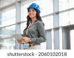 Mid adult woman architect wearing hardhat at construction site while working on digital tablet. Supervisor wearing safety helmet while working in a building site. Successful and proud inspector.