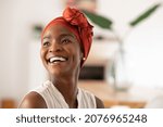 Beautiful mature black woman with african turban relaxing at home. Cheerful middle aged black woman in casual clothing with traditional headscarf at home laughing. African american lady smiling.