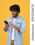 Small photo of Happy indian young man using cell phone isolated on yellow background. Smiling ethnic hipster guy holding smartphone playing game in app, dating buying online in ecommerce store on cellphone. Vertical