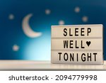 Small photo of sleeping and bedtime concept - close up of customizable light box with sleep well tonight words over moon and night stars on blue background