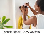 African mother measuring daughter height and marking it on wall at home. Happy black mother measuring cute little girl height at home using book and pen. Cheerful mature woman measuring her daughter.