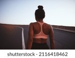 Small photo of Rearview of a young African woman in a halter top and shorts standing in the middle of a road before an early morning run