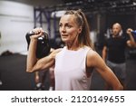 Small photo of Fit mature woman in sportswear lifting a dumbbell during a strength training session at the gym