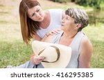 Small photo of Shot of an old lady sitting on the grass on a sunny day, feeling faint, and a young woman assisting her