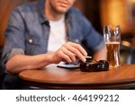 people, nicotine addiction and bad habits concept - close up of man drinking beer, smoking cigarette and shaking ashes to ashtray at bar or pub