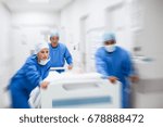 Nurse and doctor in a hurry taking patient to operation theatre. Patient on hospital bed pushed from surgeon to emergency theatre. Team of doctors and surgeon rushing patient.