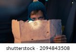 Small photo of Close Up Shot of a Caucasian Young Boy Holding the Treasure Map and a Flashlight, Looking Serious As He Tries to Decipher the Code, Sitting and Hiding in a Dark Tent During The Night.