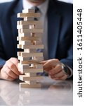 Small photo of Man business suit stacks board game wooden blocks. Close up male hands stack wooden blocks on white table. Employee develops ingenuity, sleight hand and sense balance with help board game.