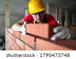 Builder carefully puts red brick on the masonry. Quick work bricklayer. Guy measures level masonry. Man is building brick wall. Correctly calculate material. Builder manually carries brick structure