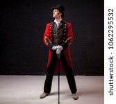 Small photo of Showman. Young male entertainer, presenter or actor on stage. The guy in the red camisole and the cylinder. Bright tailcoat, suit