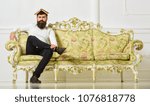 Small photo of Macho sits with open book on head, like roof. Man with beard and mustache sits on sofa, white wall background. Guy overdid with studying, fed up of reading old boring book. Overstudy concept.