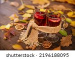 Small photo of Two glasses of hot wine wrapped in one warm scarf on wooden table background, copy space. Autumn, autumn leaves. Seasonal drink, relaxing Sunday and the concept of care, love, warmth and comfort.