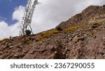 Small photo of Damaged high voltage electricity transmission tower or pivot, rock against metal, risk of landslide, material damage, poorly secured site, in a mountainous, poor and desert area, worsening and lack