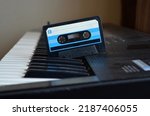 Small photo of Vintage audio tape cassette on a synthesizer keys from above,Retro cassette.Audio equipment for analog music records. Black stereo tape. Isolated plastic musical device. Old-fashioned mixtape of tunes