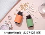 Small photo of The white pills and vitamin E capsules were poured from two unbranded pill bottles. On the table there is a glass of water, cloth towel and an alarm clock. Mockup for advertising with medicine theme.