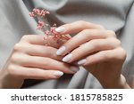Small photo of Female hands with white nail design. Female hands holding pink autumn flower. Woman hands on gray fabric background.